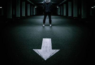 Low section of man standing by arrow symbol on road at underground parking lot