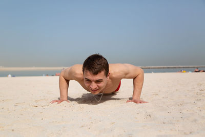 Shirtless man exercising on beach against clear sky