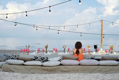 Rear view of woman sitting on furniture while looking at sea against sky