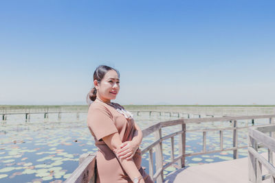 Portrait of smiling young woman on beach against clear sky