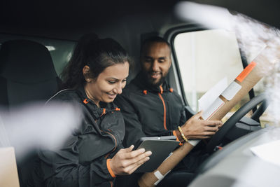 Smiling workers looking at digital tablet while sitting in delivery van