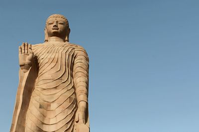 Low angle view of buddha statue against blue sky