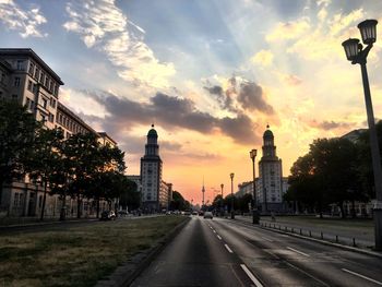 Road passing through city against sky during sunset