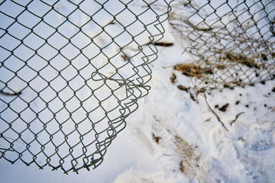 Close-up of snow on fence against sky during winter