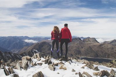 Rear view of couple standing on snowcapped mountains against sky