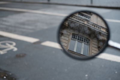 High angle view of building reflecting on side-view mirror against road