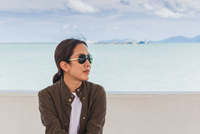 Young woman looking away while sitting by sea against sky