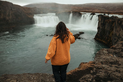 Rear view of woman standing on rock against waterfall