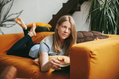 A beautiful girl is relaxing on the sofa in the living room, reading her favorite novel. 