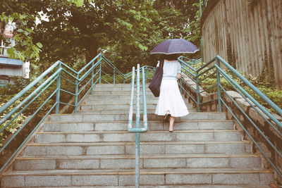 Rear view of woman carrying umbrella while walking on steps