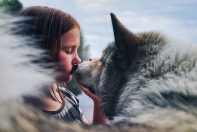 Side view of girl kissing wolf against sky