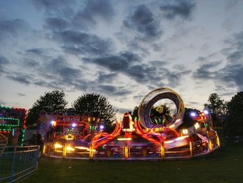 Illuminated ferris wheel against cloudy sky