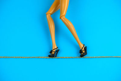 Low section of figurine walking in high heels on rope against blue background