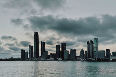 Modern buildings by river against sky in city