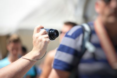 Close-up of hand holding camera against sky