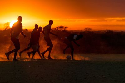 People playing soccer on field during sunset
