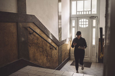 Delivery woman with package looking at phone while climbing stairs