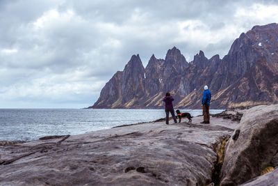 Couple with dog standing on rock at beach against cloudy sky