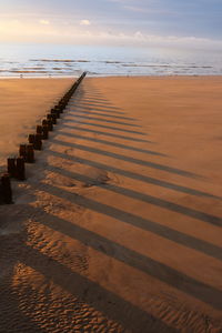 Wooden posts on beach against sky during sunset