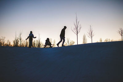 Silhouette people on snow covered land against sky during sunset