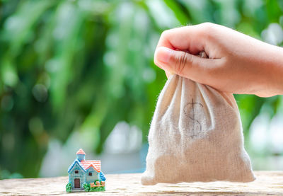 Close-up of hand holding coins in sack by model home on table