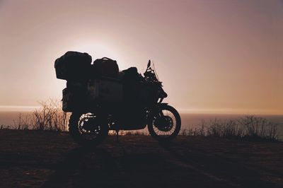 Silhouette motorcycle parked by sea against sky during sunset