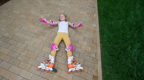 High angle view of girl wearing protection pads and roller skate lying on footpath