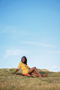 Woman sitting on field against sky