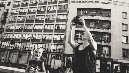 Woman photographing against building in city