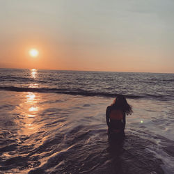Woman standing in sea during sunset
