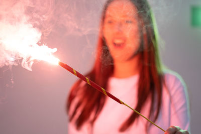 Cheerful woman holding sparkler standing against wall