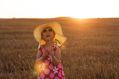 Adorable little girl in straw hat summer dress in wheat field. child with long blond hair on sunset.
