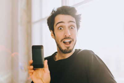 Portrait of surprised man showing smart phone at home