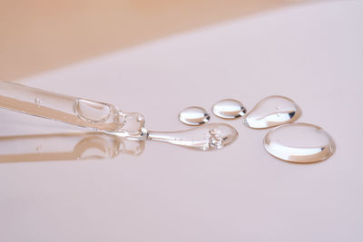 A pipette with a few drops of serum on a beige background.