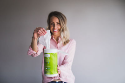 Smiling young woman holding wipes against wall