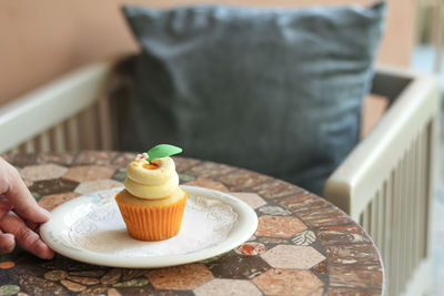 Close-up of hand holding cupcake in plate by chair