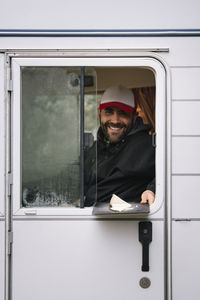 Smiling warm dressed man getting out from window and looking at camera