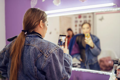 Rear view of woman taking selfie with smart phone while looking in mirror