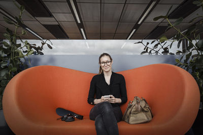 Portrait of smiling businesswoman sitting on orange couch in office