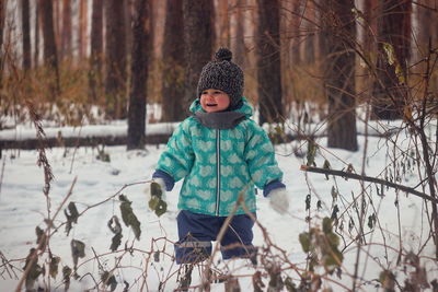 Cheerful baby girl standing in forest during winter