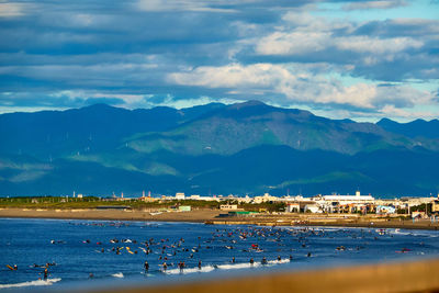 Scenic view of sea with surfers and mountains against sky in the morning
