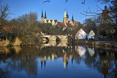 Arch bridge over river by buildings against sky