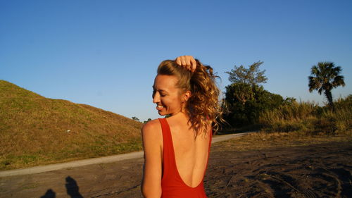 Young woman standing by tree against clear blue sky