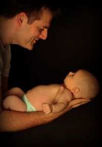 Close-up of father with baby against black background