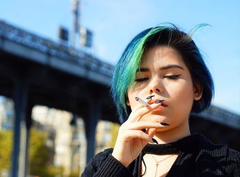 Young woman smoking cigarette against bridge