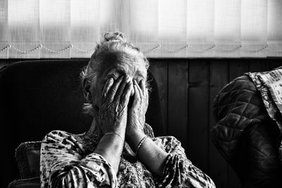 Mature woman with hands covering eyes sitting at home