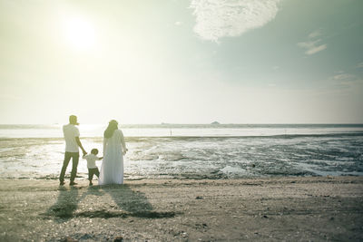 Happy family standing on shore at beach against sky