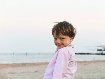 Portrait of cute boy standing on beach against sky