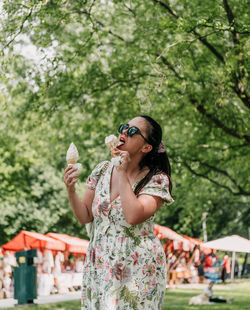 Portrait of young woman eating two ice cream cones in park in city