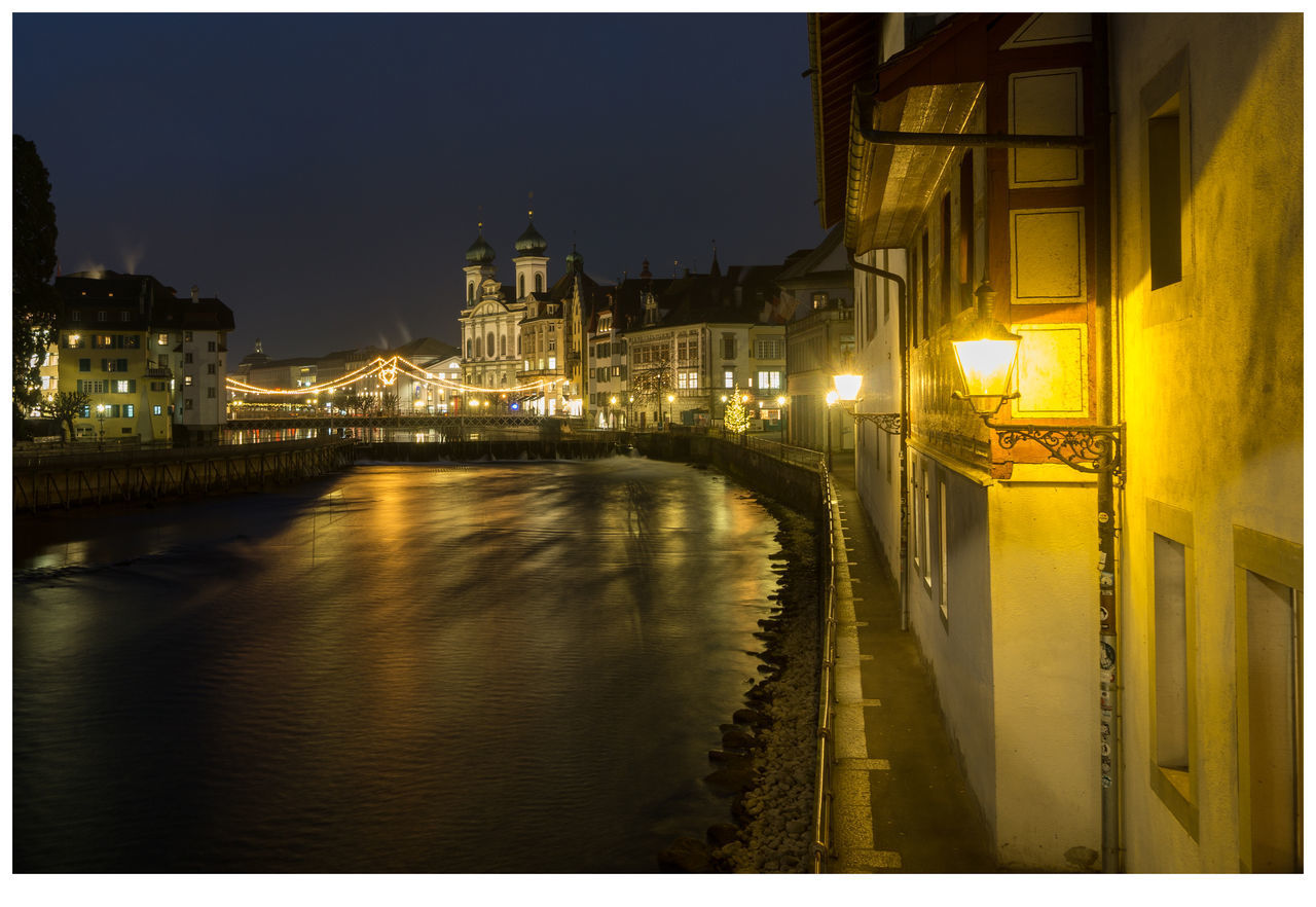 ILLUMINATED BUILDINGS BY RIVER AGAINST SKY